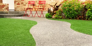A curved gray stone path leads to a porch with two red chairs and green grass