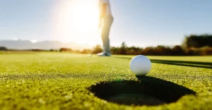 A golf ball near a hole on green grass with a person in the background