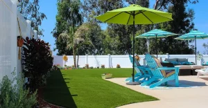Patio with green grass, blue chairs, and umbrellas under sunny sky with trees in the background