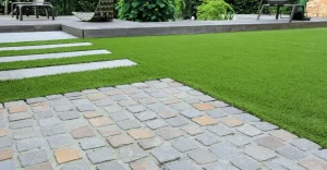 A garden scene with green grass, stone walkway, and a patio in the background