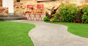 A curved stone pathway leads to two red chairs near a brick wall and greenery