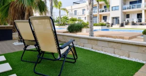 Two reclining chairs on a lawn next to a swimming pool and buildings
