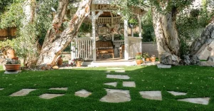 A gazebo surrounded by trees and potted plants, with stone pathways on green grass