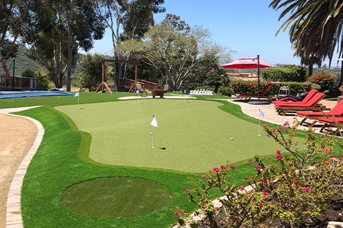 A green putting area with flags, surrounded by landscaping and lounge chairs