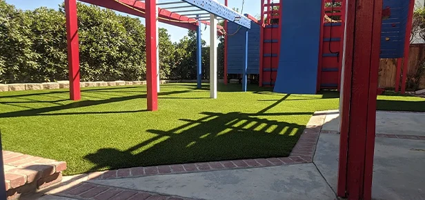 Playground with artificial grass, red and blue structures, and a paved walkway