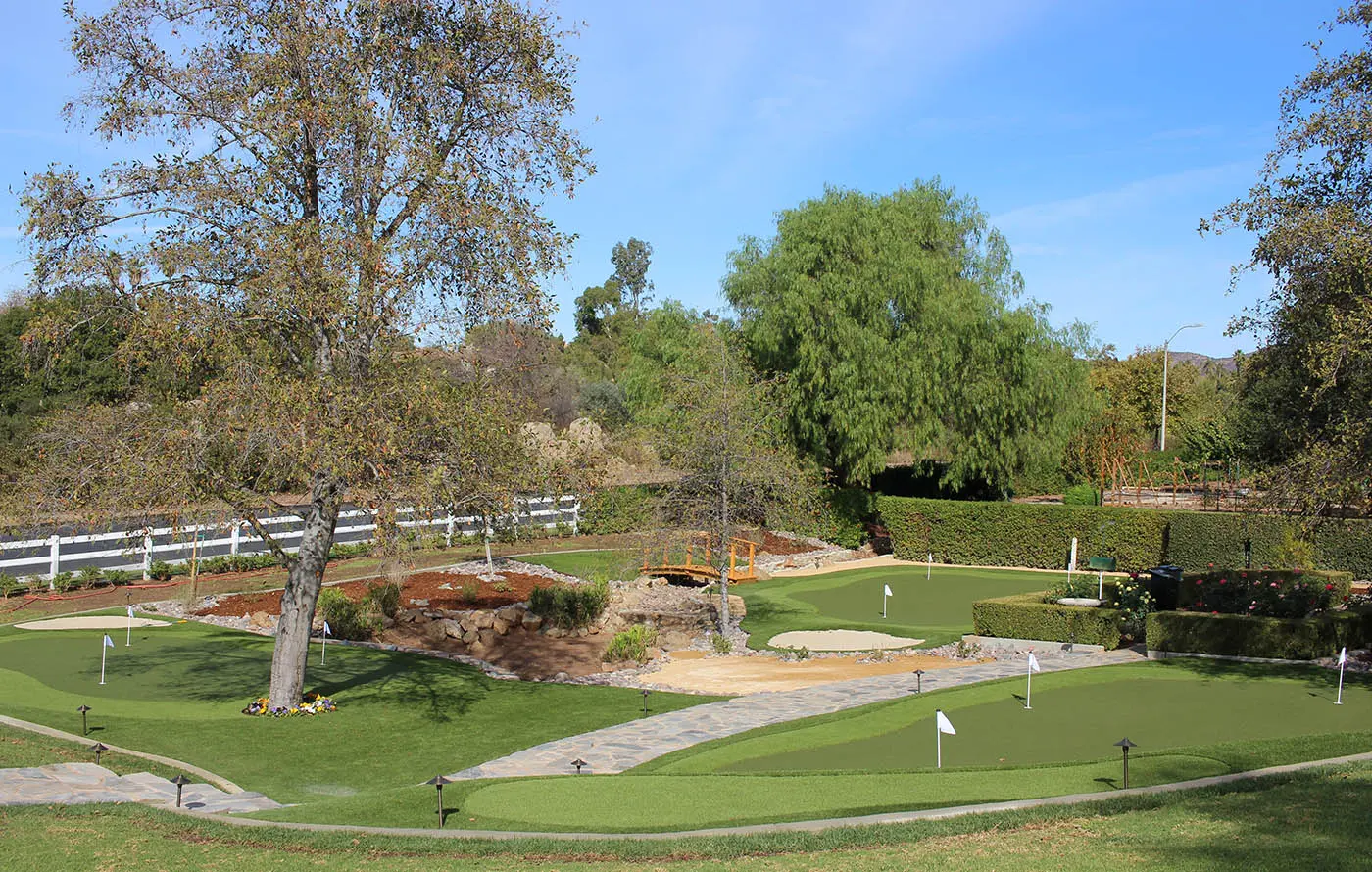 A landscaped area with grass, trees, and a small pathway. Clear blue sky above