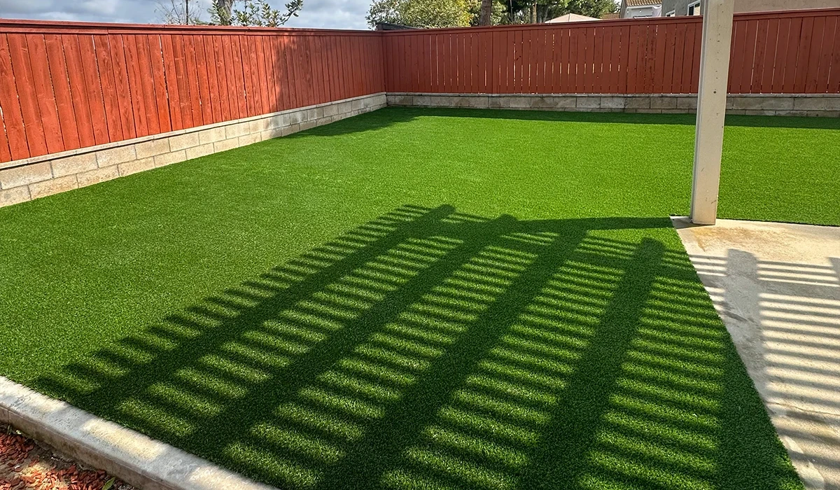 Artificial turf lawn with a shaded area from a pergola and a wooden fence in the background