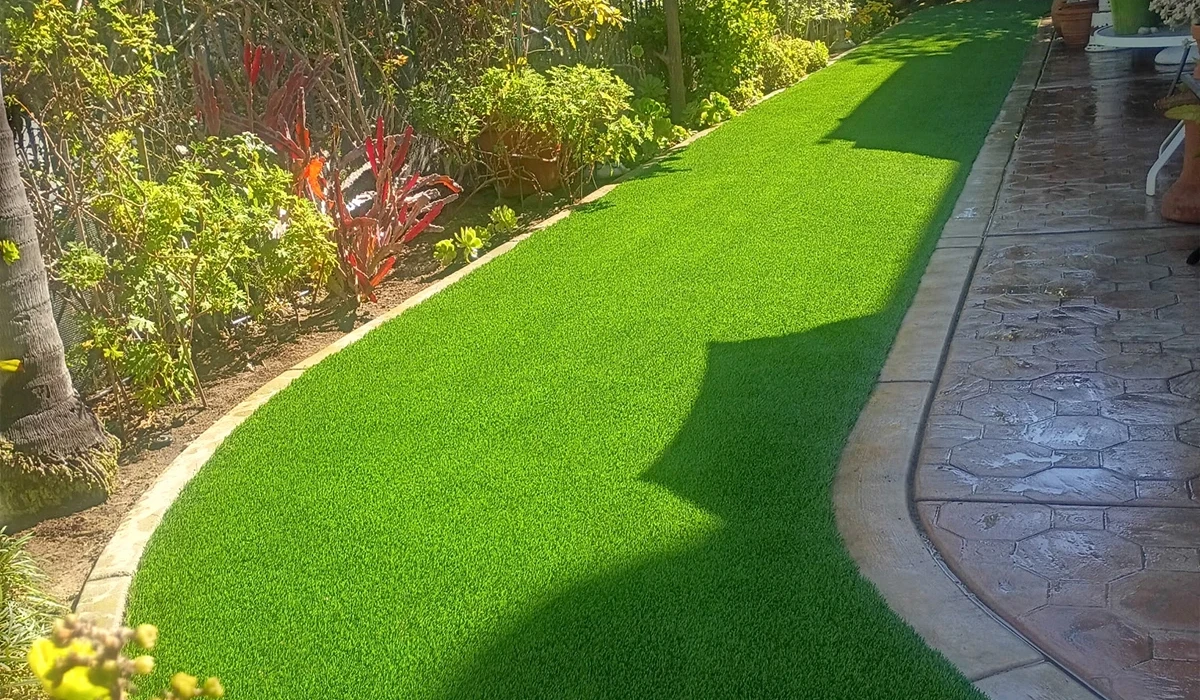 Artificial grass path lined with flowers and plants in a garden
