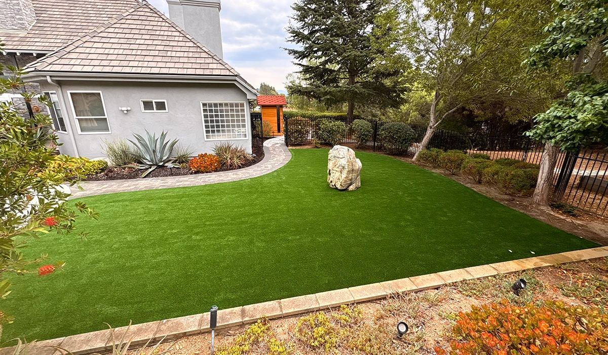 Backyard with artificial grass, a rock feature, and surrounding trees and plants