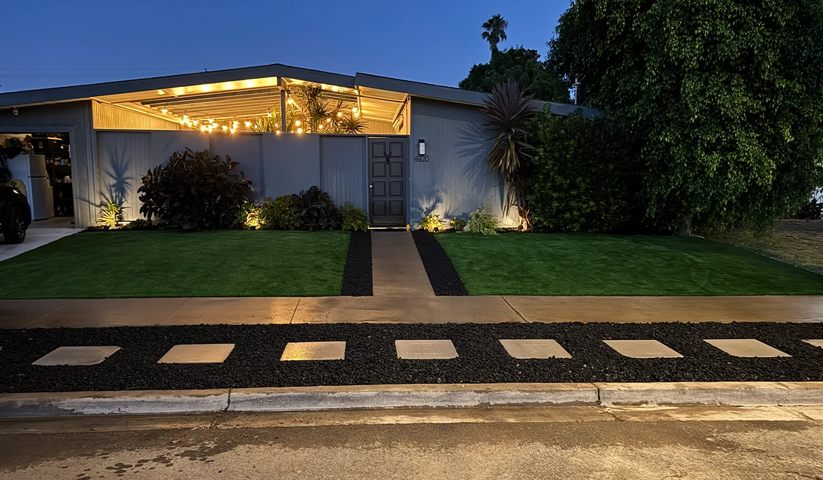 A modern house with a front lawn, pathway, and outdoor lighting at dusk