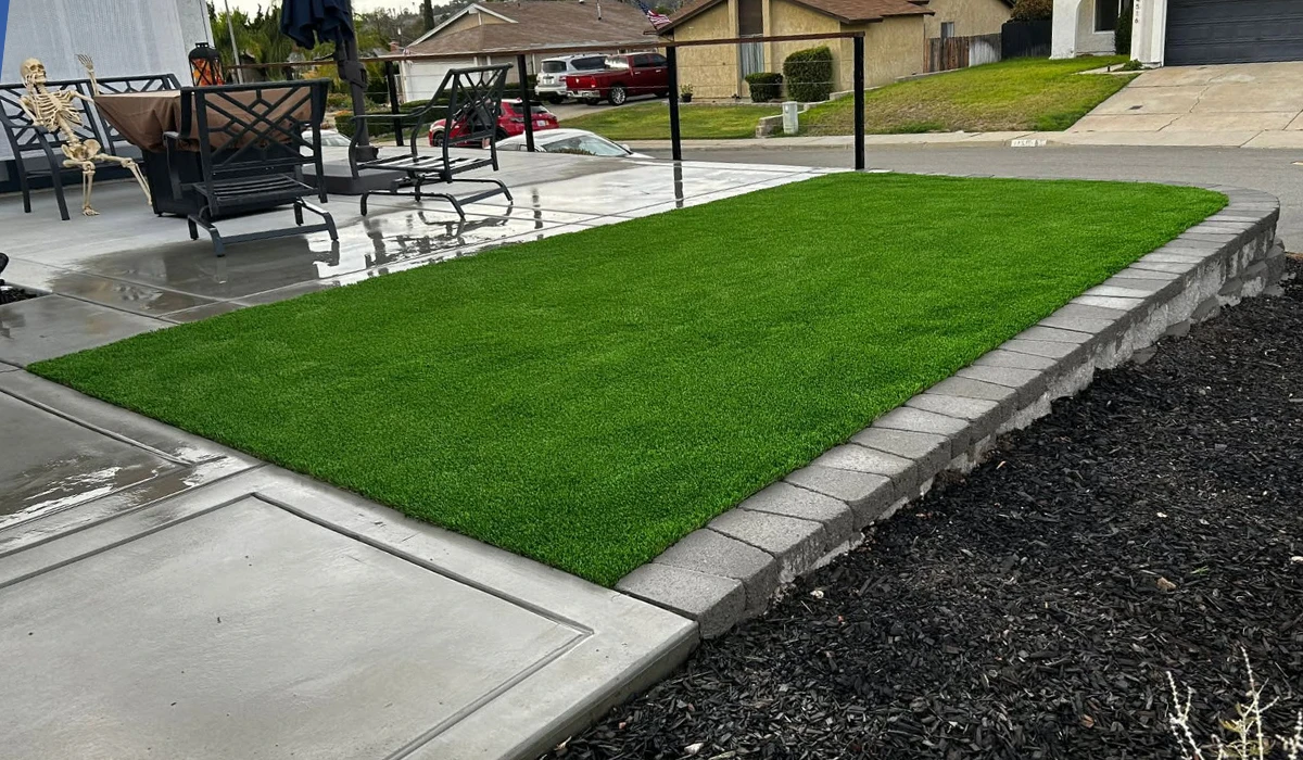 A patch of artificial grass bordered by a concrete slab and gravel