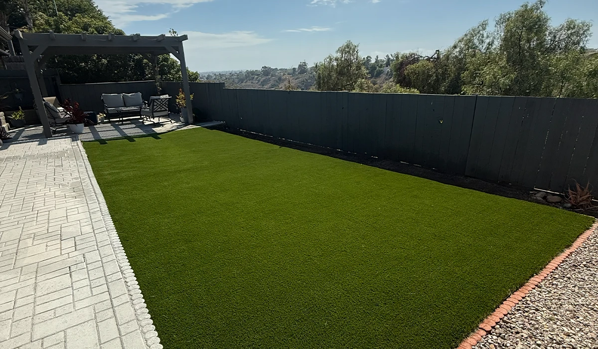 Lawn area with artificial grass and a stone border, viewed on a sunny day