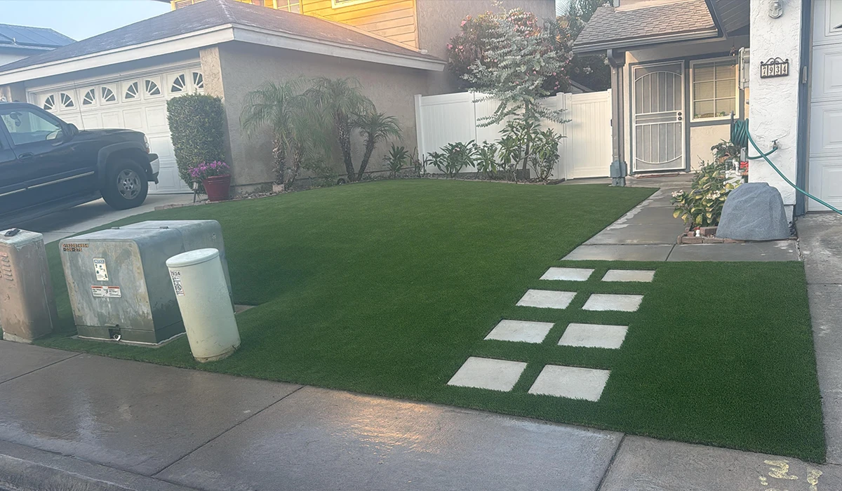 Front yard with artificial grass, stone pathway, trash can, and plants by a house