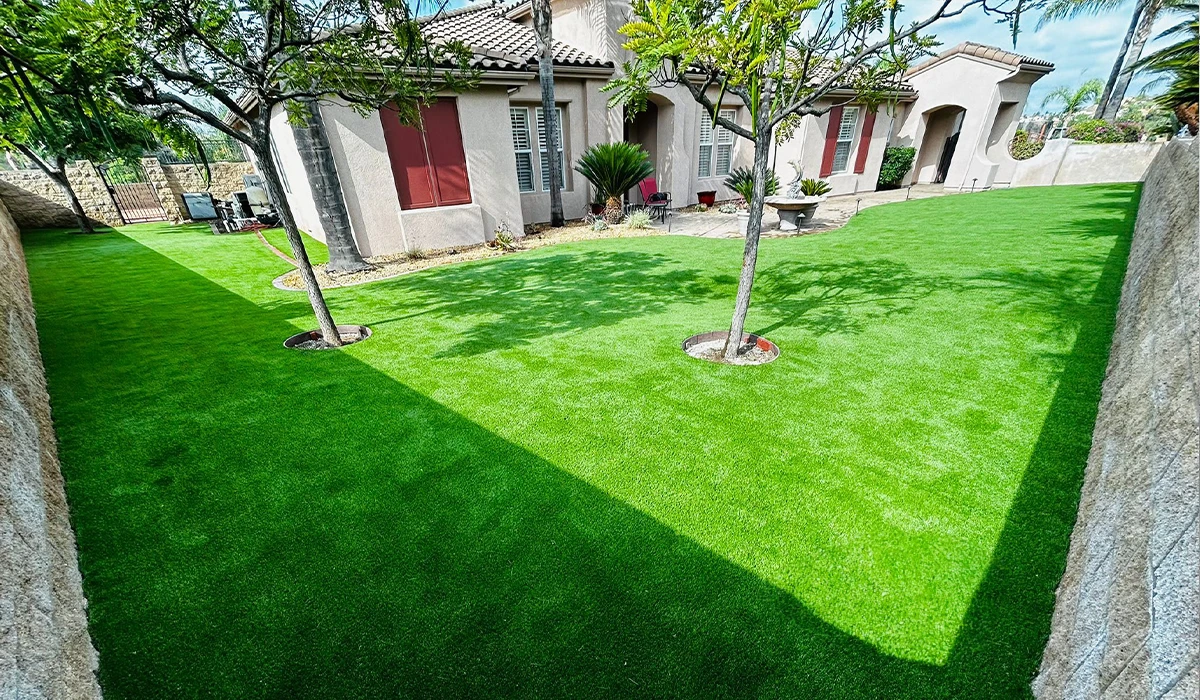 Green artificial turf in a backyard with trees and a house in the background