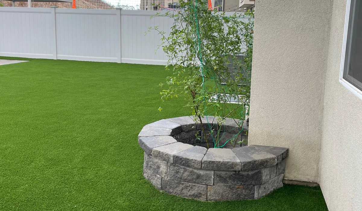 A planted tree near a stone circular bench on artificial grass