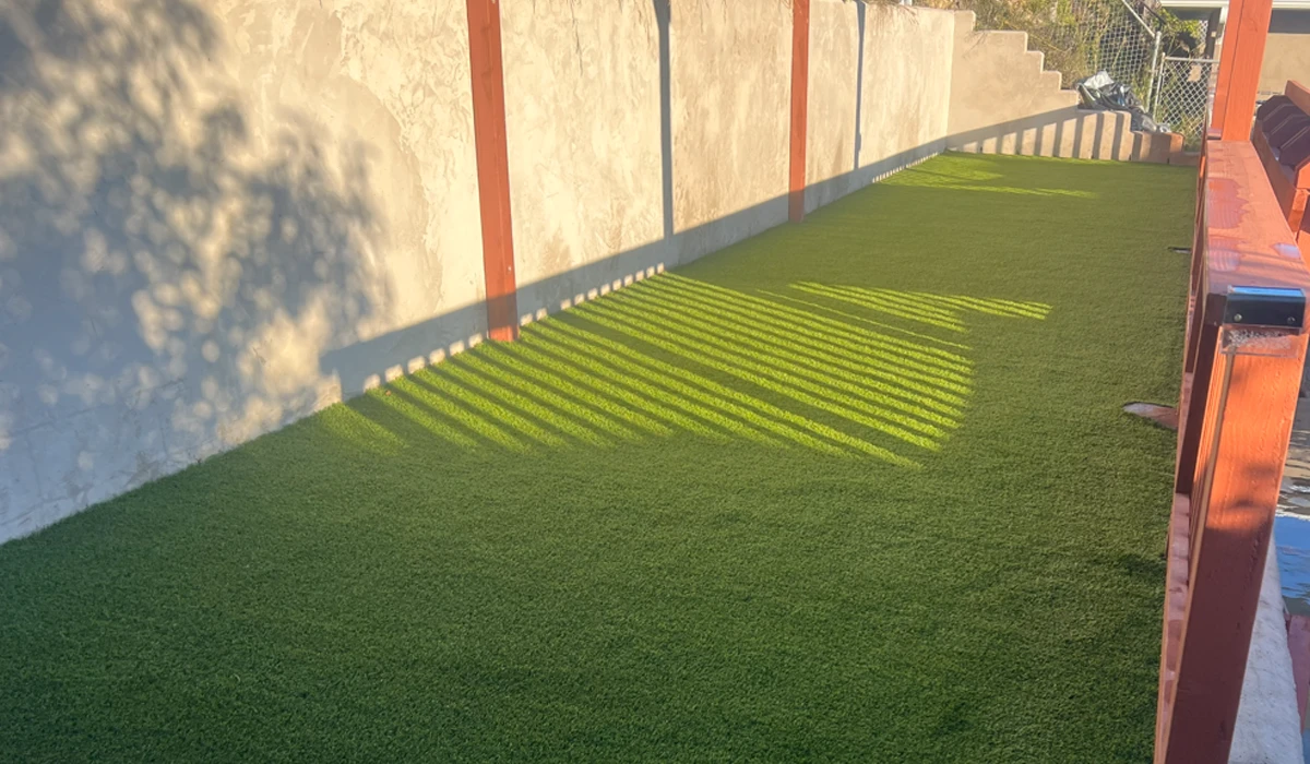 Artificial green grass area beside a wall, with shadows from nearby structures