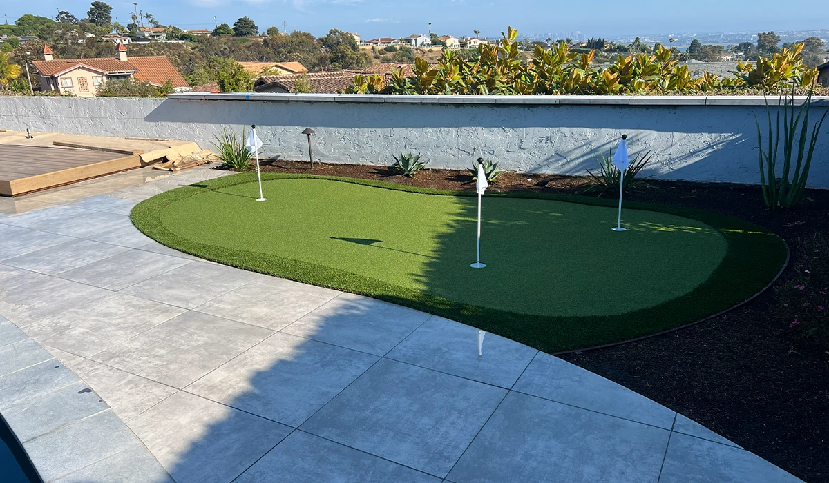 A backyard with a green artificial putting green, surrounded by concrete and landscaping
