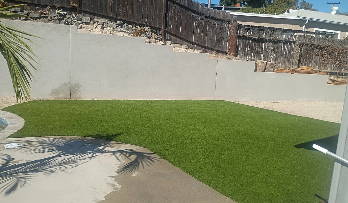 View of a backyard with green artificial grass and a gray wall in the background
