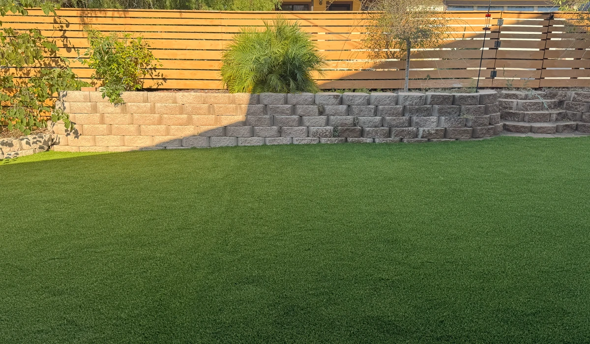 Green artificial grass yard with stone steps and a wooden fence in the background