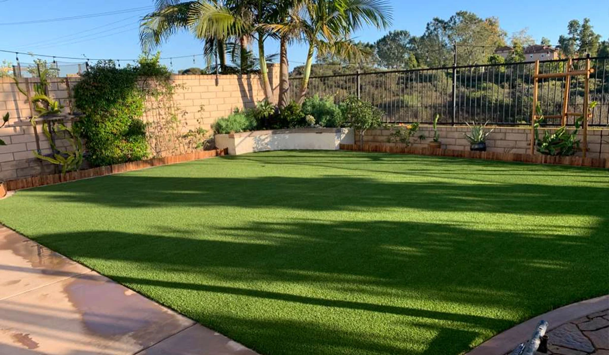 A green artificial lawn surrounded by plants and a stone wall