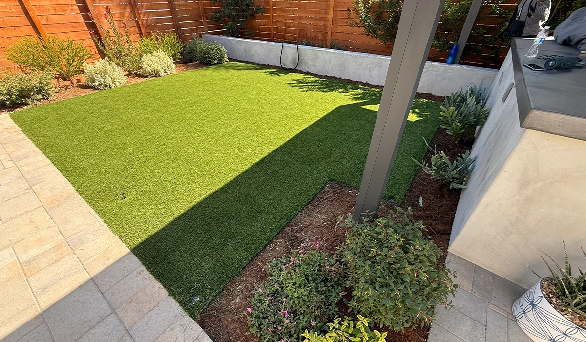Lawn area with artificial grass, surrounded by plants and a concrete border
