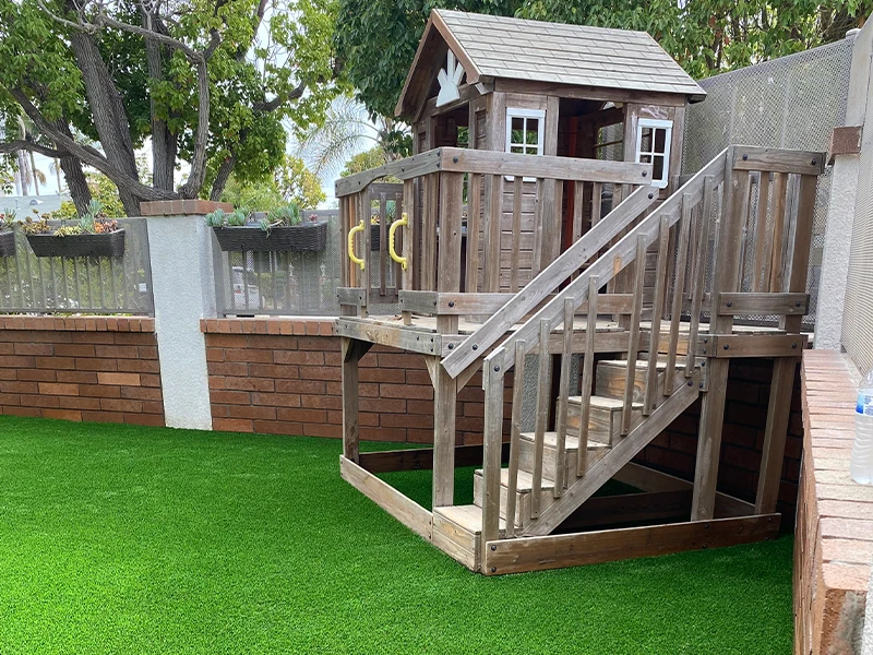 Wooden playhouse with stairs on artificial grass in a fenced yard
