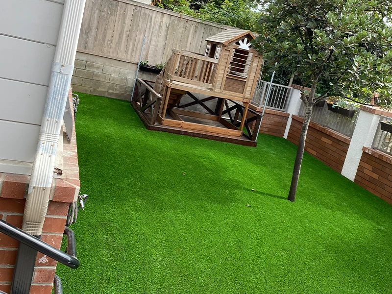 Backyard with artificial grass, wooden play structure, and surrounding fences
