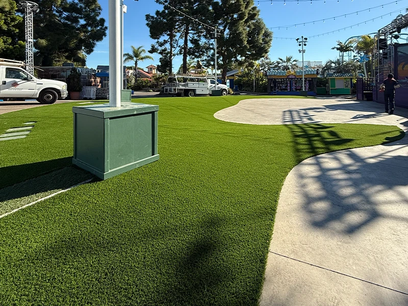 A landscaped area with green artificial grass and a concrete path, surrounded by trees
