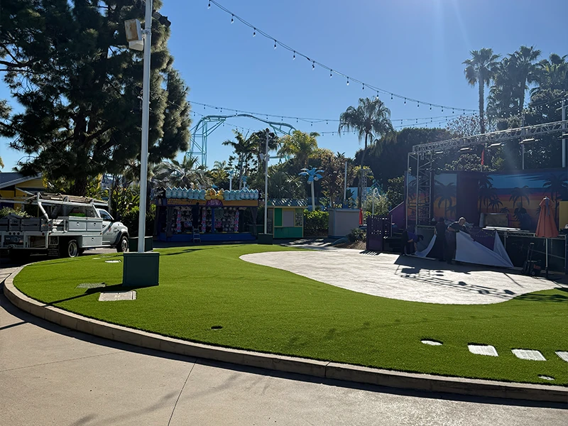 An outdoor area with artificial grass, stage equipment, and palm trees under a clear sky