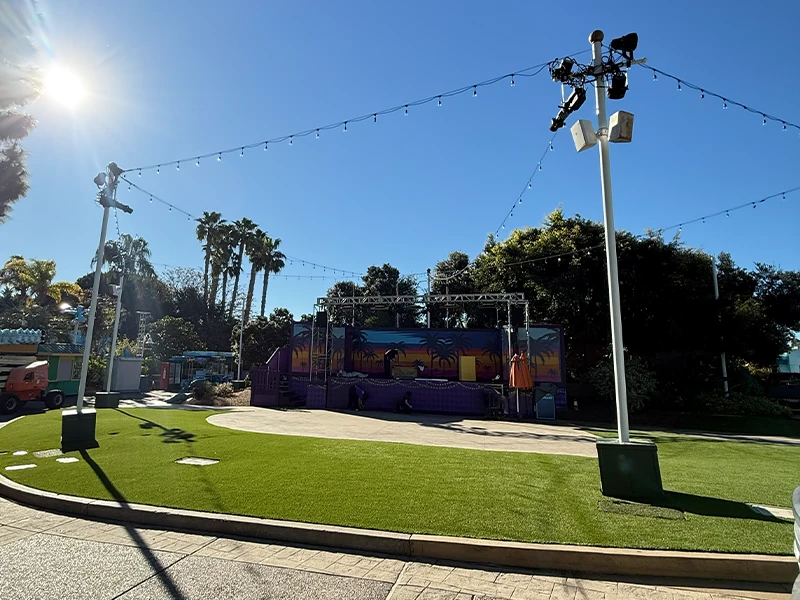 An empty outdoor stage area with lights and palm trees in the background