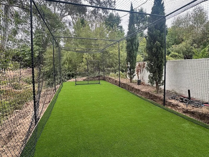 A fenced area with artificial grass and a goalpost surrounded by trees