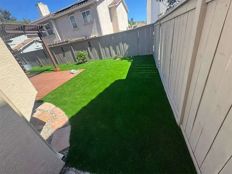 View of a backyard with green grass, a stone path, and a wooden fence