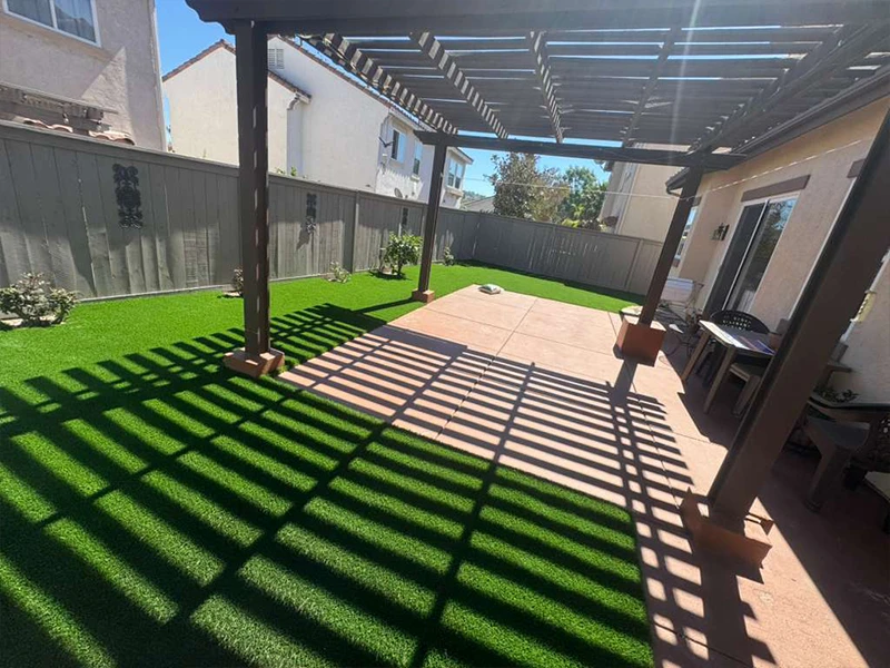 Patio with artificial grass under a pergola, with shadows on the ground