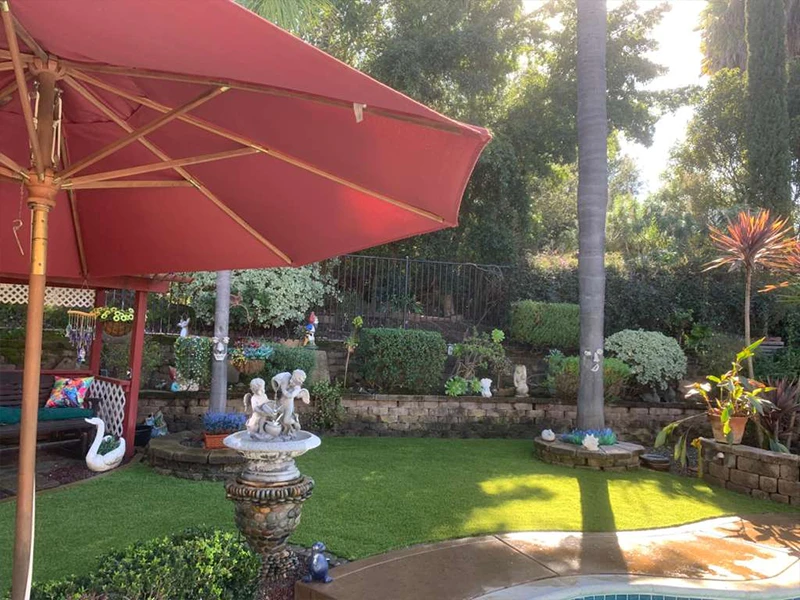 Garden scene with a red umbrella, grass, statues, and various plants