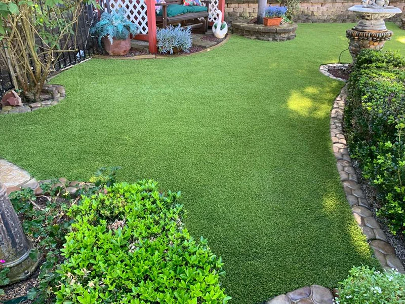 Lush green lawn with garden beds and stone pathways, featuring a shaded seating area