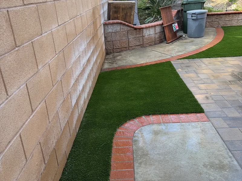 View of a landscaped area with grass and a brick pathway beside a wall