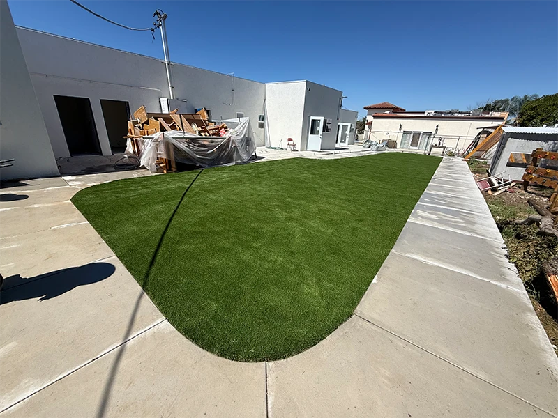 A green artificial lawn in a courtyard area surrounded by white walls and concrete