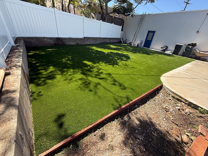 Artificial grass lawn bordered by a concrete path and a white fence