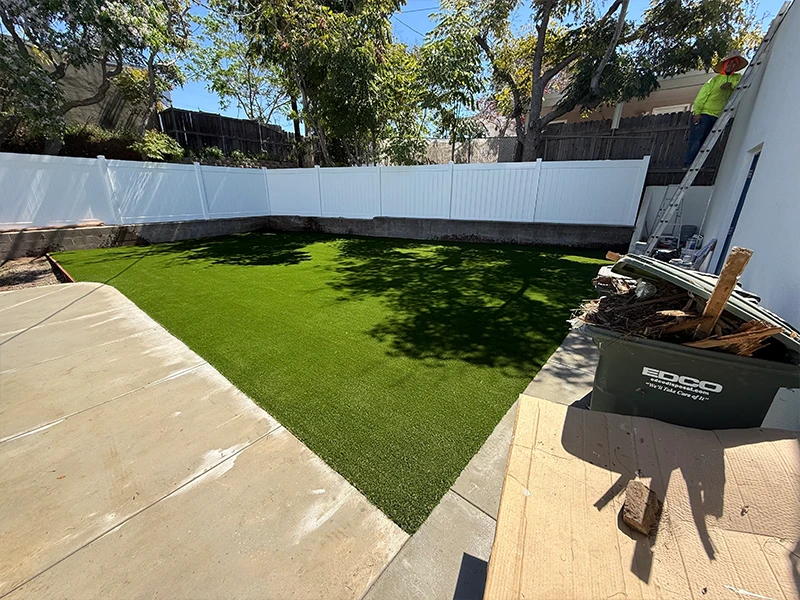 View of a backyard with artificial grass and a white fence on two sides