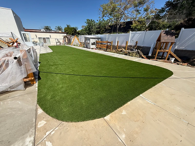 Green artificial turf on a patio with construction materials in the background