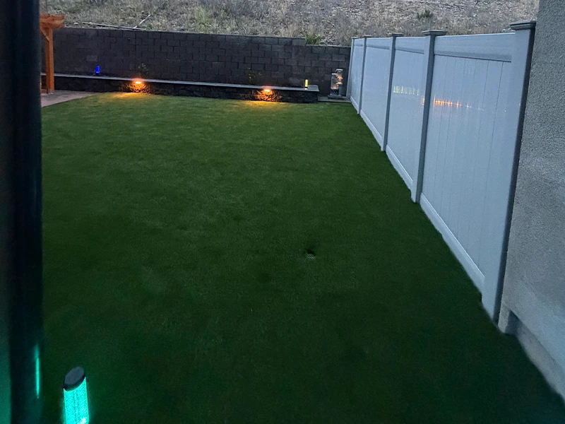 A grassy backyard with a white fence and low outdoor lighting