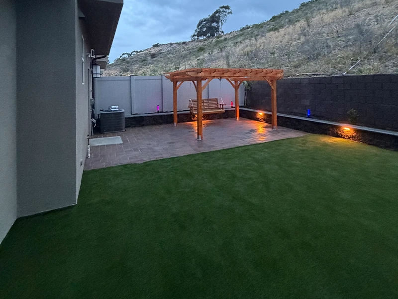 View of a backyard with artificial grass, a wooden pergola, and dim lighting