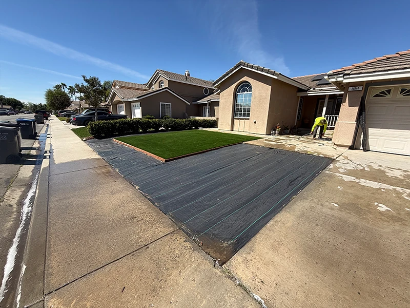 Concrete driveway with freshly laid sod in a residential area, under clear blue sky