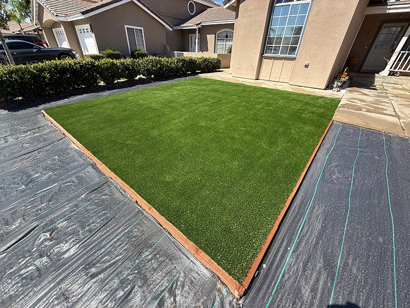 A grassy area with artificial turf bordered by a wooden frame next to a house
