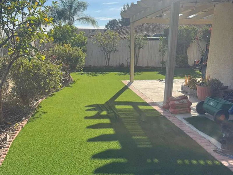 A garden with artificial grass, plants, and a patio area under a pergola