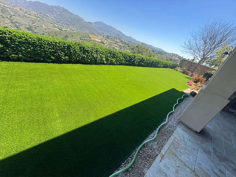 Green artificial lawn with mountains in the background and a clear blue sky