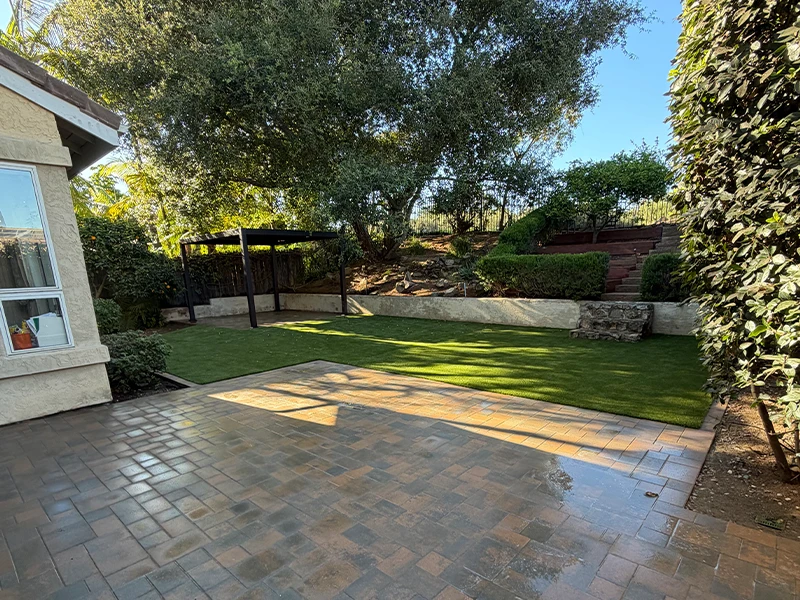 A patio area with grass and trees, along with a stone wall and shaded seating