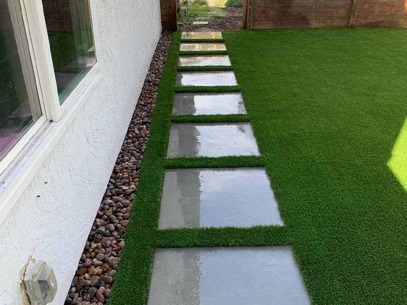 Concrete stepping stones on artificial grass beside a house wall