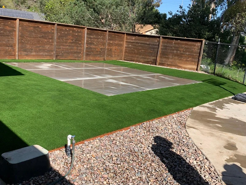 A backyard featuring artificial turf, a paved area, and a wooden fence