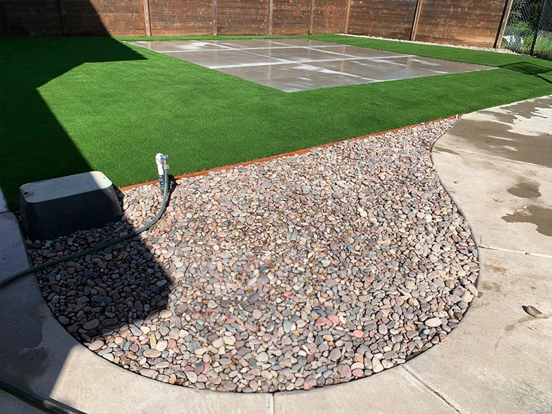 A backyard with artificial grass, a gravel area, and a concrete patio